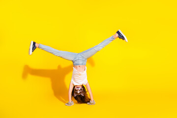 Little girl performing handstand on yellow background wearing animal mask in casual outfit showcasing quadrobica trend and playful spirit
