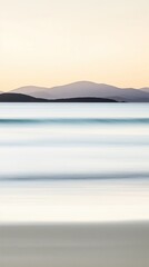 Fototapeta premium Serene coastal view with blurred ocean waves and distant mountains under soft evening light