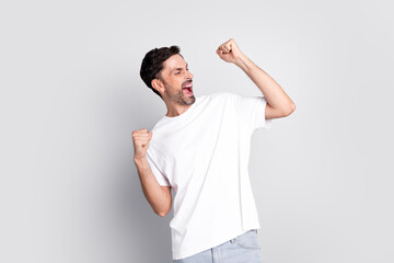 Cheerful young man in casual white t-shirt celebrating with fists raised, expressing excitement and...