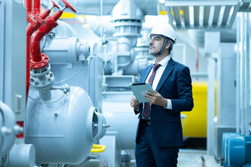 Professional inspecting industrial facility equipment while holding a tablet and wearing a hard hat during work hours