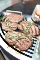 A beef steak from marbled beef seasoned with sprigs of rosemary is cooking on the grill surface. The grill is in the backyard of your chalet. Outdoor
