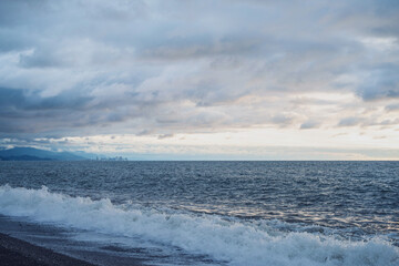 Fototapeta premium Beautiful seascape with Batumi city on the horizon in the evening. Black wavy sea, disturbing cloudy sky, clouds, mountains.
