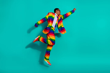 Charismatic young man in vibrant rainbow-striped suit posing dynamically on turquoise background