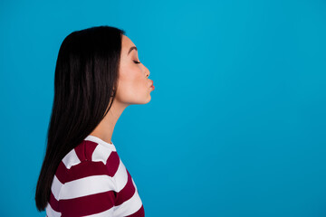 Side profile of young woman pursing lips playfully against a vibrant blue background