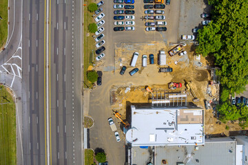 Panoramic view of construction site with machinery surrounded by parked cars next to busy road near...
