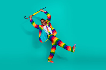 Charismatic man in colorful striped suit posing with umbrella on vibrant turquoise background.