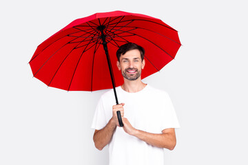 Cheerful young man holding a bright red umbrella, wearing a casual white t-shirt against a grey...