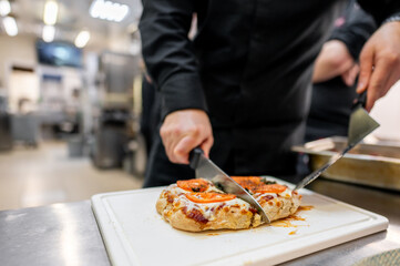 A chef skillfully slices a freshly baked pizza on a cutting board in a commercial kitchen, showcasing delicious toppings and a crispy crust.