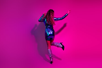 Stylish girl in glossy blue dress dancing against vibrant pink background, radiating glamour and confidence