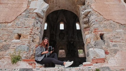 A content creator in an old stone building reviews her recent shots, her smile reflecting excitement for storytelling in a historic setting,she glances at the camera capturing her and smiles.