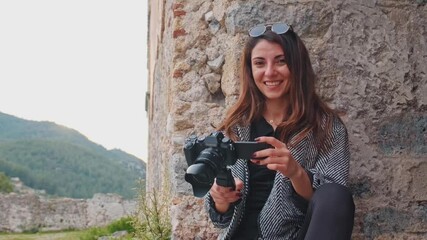 A content creator in an old stone building reviews her recent shots, her smile reflecting excitement for storytelling in a historic setting,she glances at the camera capturing her and smiles.