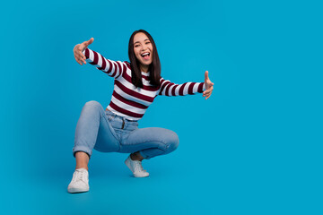 Smiling young woman with outstretched arms posing joyfully against a vibrant blue backdrop