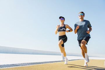 Couple jogging on a sunny day along a coastal walkway in athletic gear enjoying their fitness routine