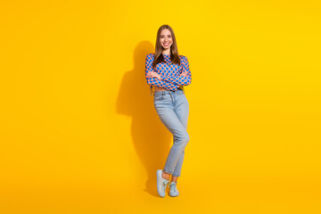 Trendy young woman standing against a vivid yellow background, wearing a stylish patterned shirt...