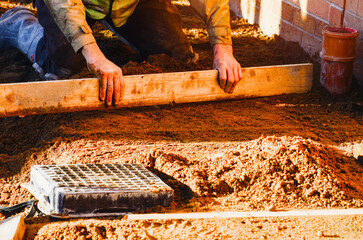 Construction worker levels sand for a foundation in a sunny outdoor setting during the day,...