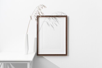 Blank portrait picture frame mockup on white wall with botanical decor in vase, copy space