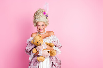 Fototapeta premium Elegant woman in a historical costume holding a teddy bear against a pink background