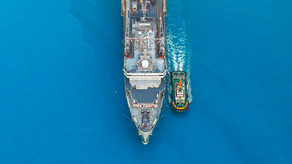 Aerial view tugboat pushing aircraft carrier at sea.
