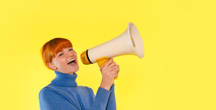 Young woman enthusiastically speaking into a megaphone against a vibrant yellow background, showcasing energy and passion