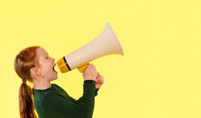 Young girl enthusiastically using a megaphone against a bright yellow background during a playful...