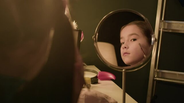 Closeup of Asian child actress standing in front of mirror in theatre dressing room, doing makeup