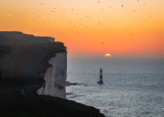 Sunrise behind beachy head lighthouse during hide tide on the south downs east Sussex south east...