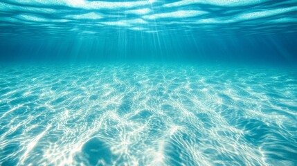 Sunlit underwater scene with rippling sand and clear blue water.