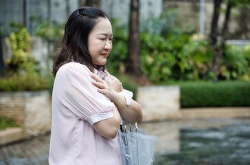 Asian middle-aged woman holding umbrella after raining, sick Asian aunt having cold, flu, fever,...