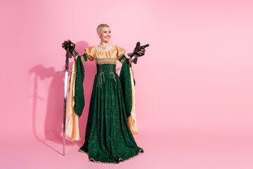 Fototapeta premium Elegant woman in medieval costume with sword against pink background