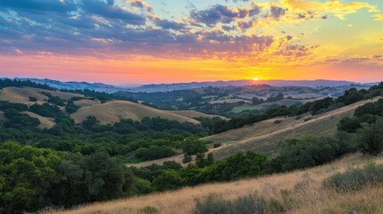 Fototapeta premium A dramatic sunset sky with layers of vibrant colors blending into the horizon over rolling hills.