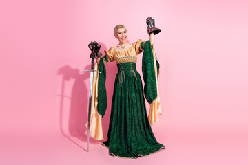 Fototapeta premium Elegant woman in medieval costume holding props and posing on pink studio background