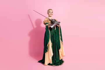 Fototapeta premium Elegant young woman dressed as a medieval queen, holding a sword against a bright pink background