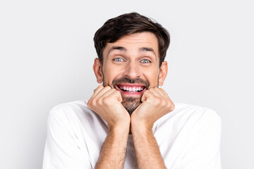 Excited young man expressing happiness with hands under chin in casual white shirt on gray...