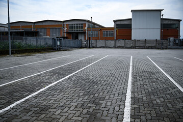 Fototapeta premium Parcheggio in pavimentazione autobloccante con segnalatica bianca con edificio industriale sullo sfondo