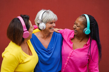 Happy multiracial senior women listening music with wireless headphones in the city - Trendy elderly people enjoy day outdoor