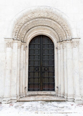 An old black metal door is in white wall of an ancient church, front view