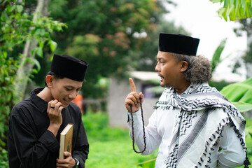 Young Indonesian Muslim male student wearing a skullcap studying with an ustadz, Ramadhan concept.
