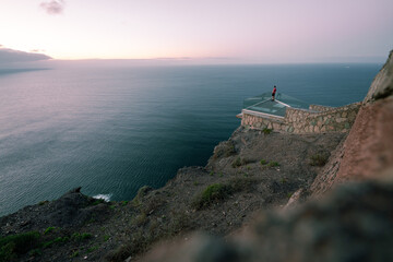 Osoba na szklanym tarasie widokowym nad klifem o zachodzie słońca © Adam.rtk