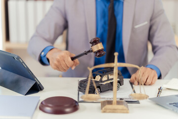 Judge and miniature car symbolize auction or court action against driver who has accident and receives insurance payment, car with scale and hammer on table