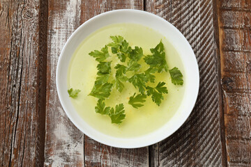 Tasty chicken bouillon with parsley in bowl on wooden table, top view