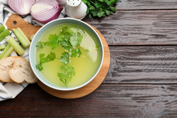 Tasty chicken bouillon in bowl, bread and ingredients on wooden table, flat lay. Space for text