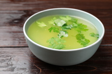Tasty chicken bouillon in bowl on wooden table, closeup