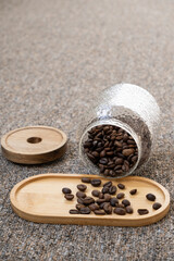 Roasted coffee beans in a glass jar collapsed on a wooden stand on a carpet