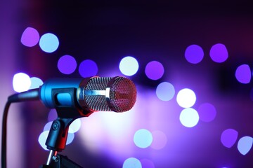 Obraz premium Microphone on stand against color background with blurred lights, space for text. Bokeh effect