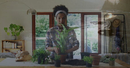 Image of landscape over biracial woman nurturing plant at home