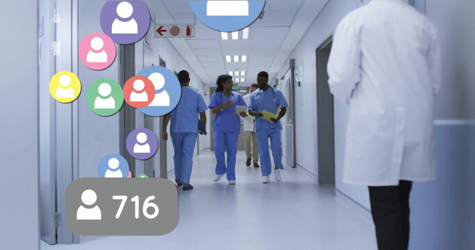 Image of media icons over diverse doctors walking and talking in hospital