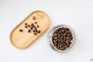 Roasted coffee beans in a glass jar and wooden stand. White background. Top view