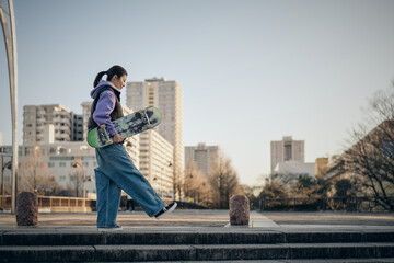 スケートボードを抱えて公園を歩く女性 © monzenmachi