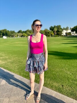 Jeune femme en top fuchsia et mini-jupe bleue devant un gazon