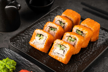 Crispy sushi rolls on black plate with soy sauce and wasabi